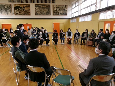 小学校の体育館で行われたPTA総会にて、部会ごとに円形に並べられたパイプ椅子に座って会議を行う、大勢の保護者の様子を写した写真