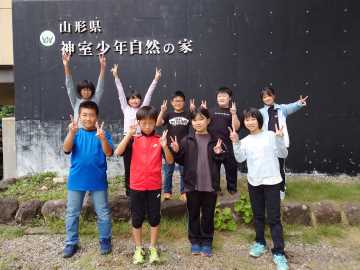 神室少年自然の家と書かれた壁の前で思い思いのポーズをとる児童たちの写真