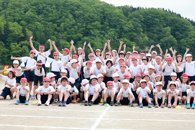 手を挙げたりピースサインをしたりする児童たちの集合写真