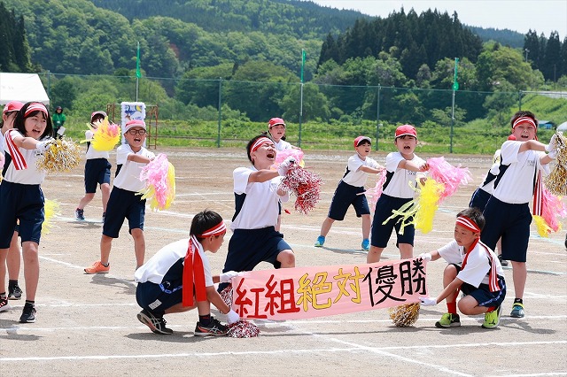 「紅組絶対優勝」の横断幕を持ち、声を張って応援する紅組児童たちの写真