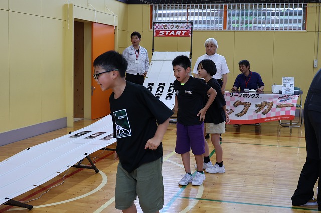 体育館に作られたモックカーのレース場で自分の作った車の走行具合を見る男子児童の写真