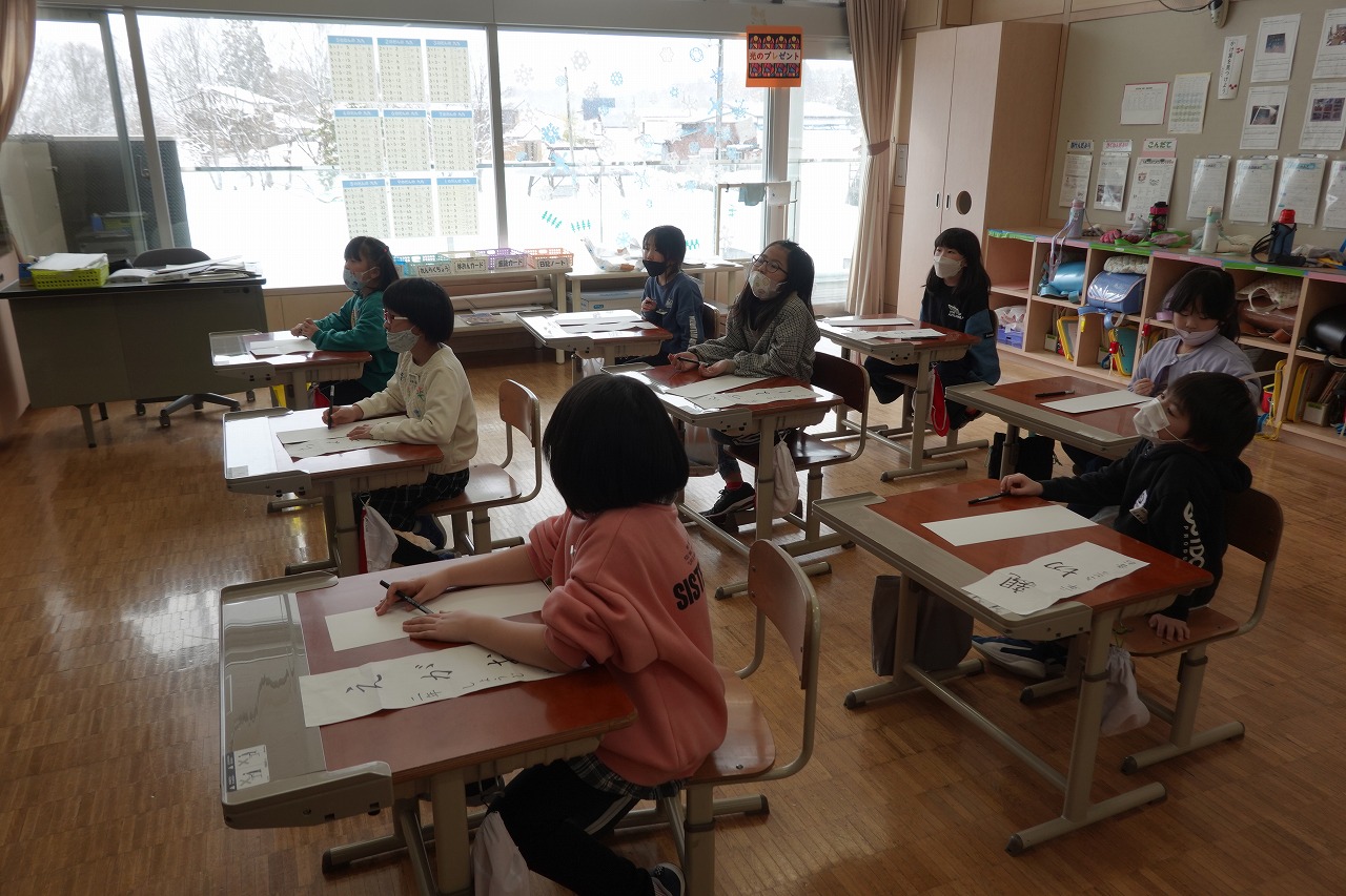 机に座りながらペン習字をする生徒たちの写真