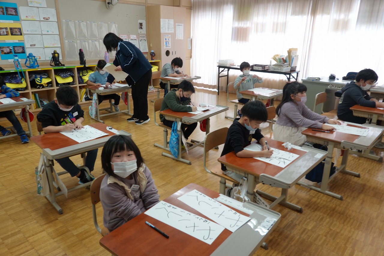 ペン習字を先生に見てもらいながら練習に打ち込む生徒たちの写真