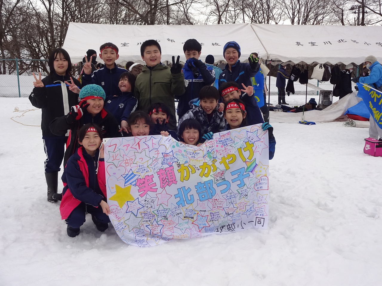 秋山スキー場で開催されたスキー大会にて、真室川北部小学校の待機場の前で14人の児童が、「笑顔かがやけ北部っ子」と書かれた応援旗を掲げながらポーズを取って撮影された記念写真
