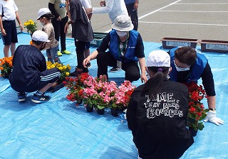 ブルーシートの上で花の手入れをする、児童たちと人権擁護委員の方々の写真