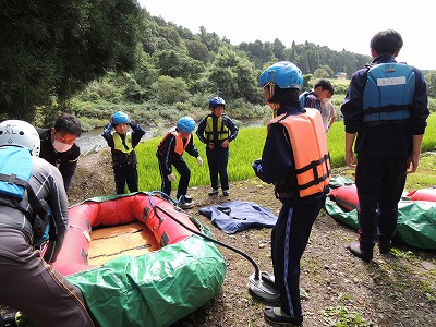 橙色や黄色の救命胴衣を身につけて、ゴムボートの周囲に集まった児童たちの写真