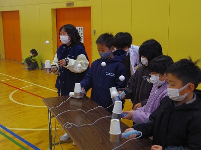 紙コップなどで出来た装置を実際に試用してみる児童たちの写真