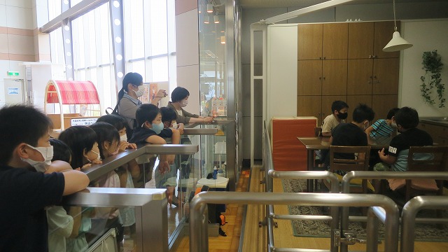 校外学習にて、山形県防災学習館の施設内にある地震装置を体験する3年生の児童4人と、それを見学する残りの児童達の様子を写した写真
