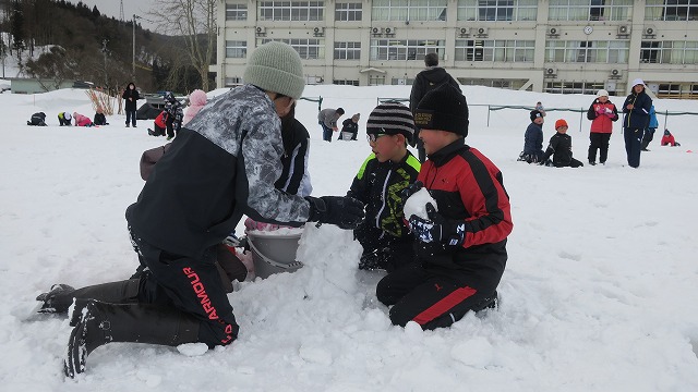 雪を固めて積み上げている、4人の児童たちの写真