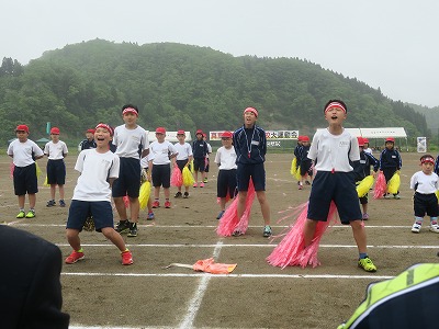 赤いハチマキに赤と黄色のポンポンを手に持って声の限りに応援をする紅組児童たちの写真