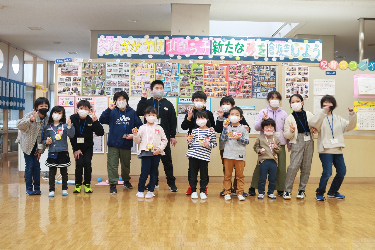 小学校の教室内で行われた新入生体験入学にて、5年生と入学前の児童達が、掲示板の前に並んでピースサインをして撮影された記念写真
