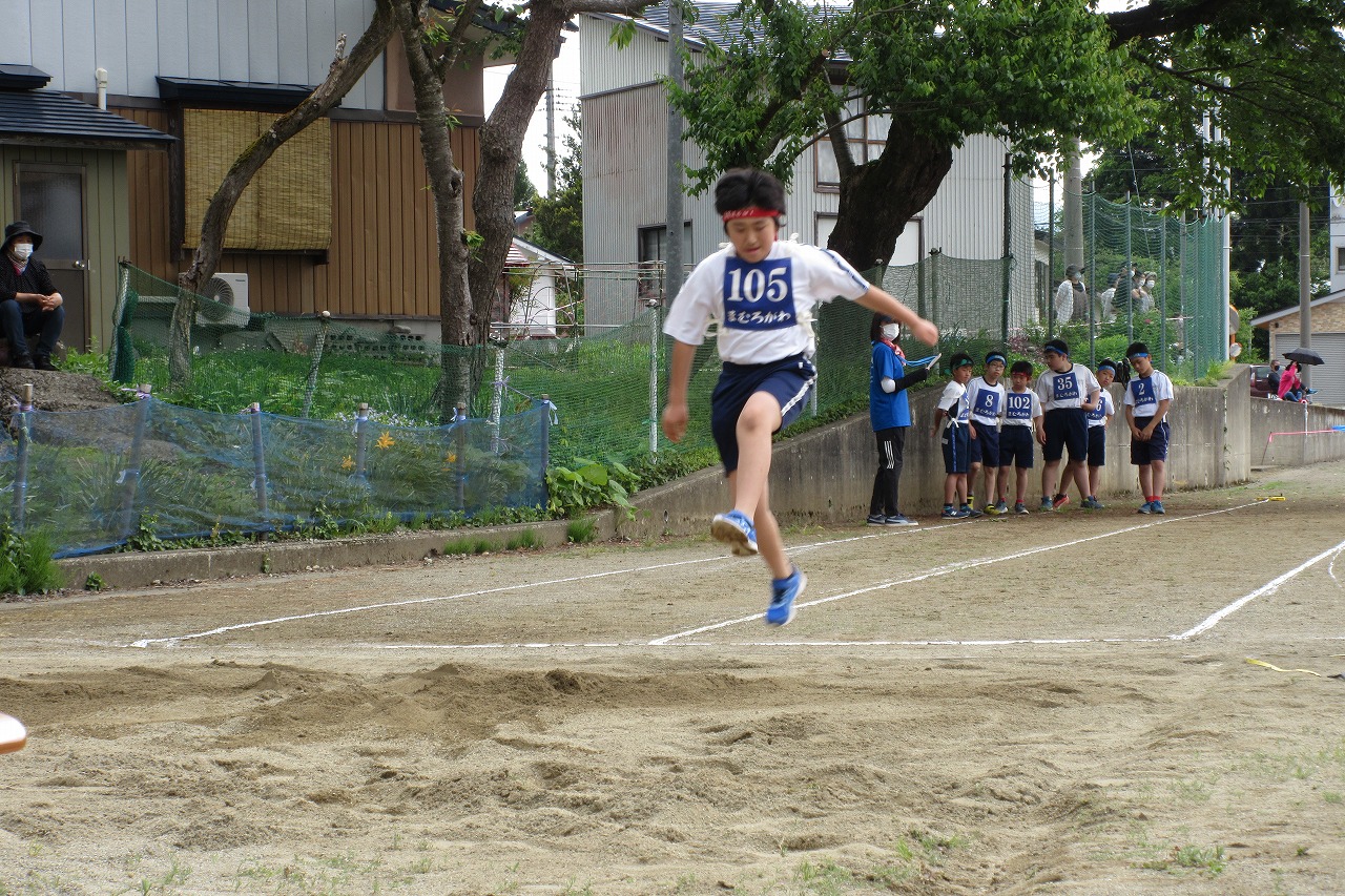 走り幅跳びで105番のゼッケンを着けた男子児童が右足で踏み切って飛びあがっている様子の写真