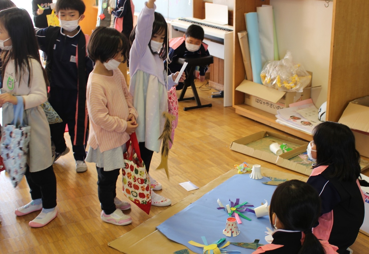 紙コップなどで作ったおもちゃの前に座る子供たちの前で勢いよく紙のおもちゃを引き上げる子供の写真
