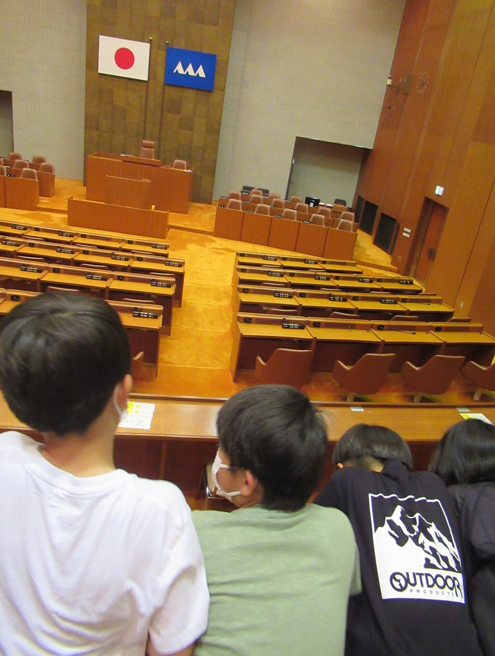 日本国旗と山形県旗が飾られた議会を見学する子供たちの写真