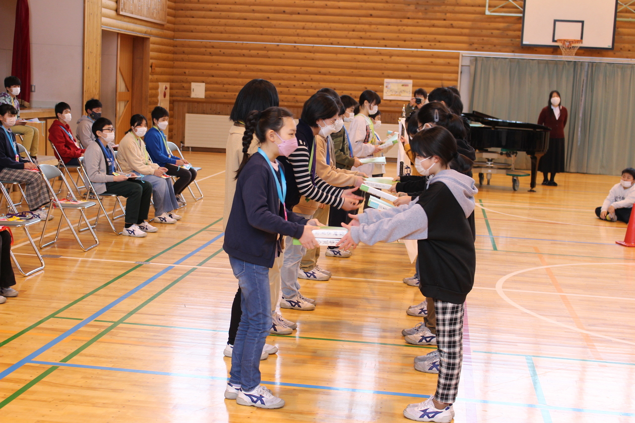 子供たちが2列に向き合って並び、2冊の本を手渡ししている写真