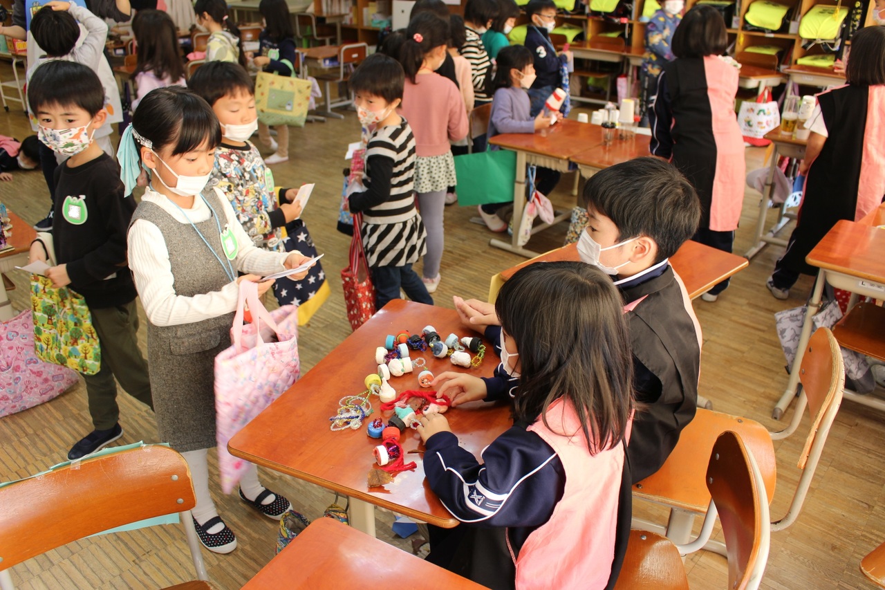 ペットボトルのキャップを使ったおもちゃを並べている二人の子供の前に立つ女の子の写真