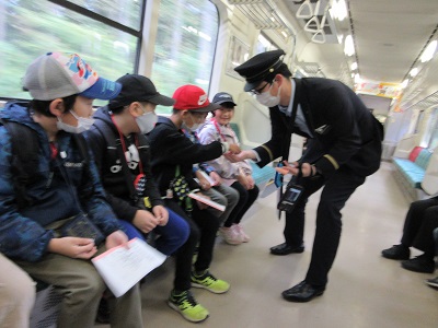 電車の座席に座った子供たちと、制服を着た車掌が子供たちの切符を確認している写真