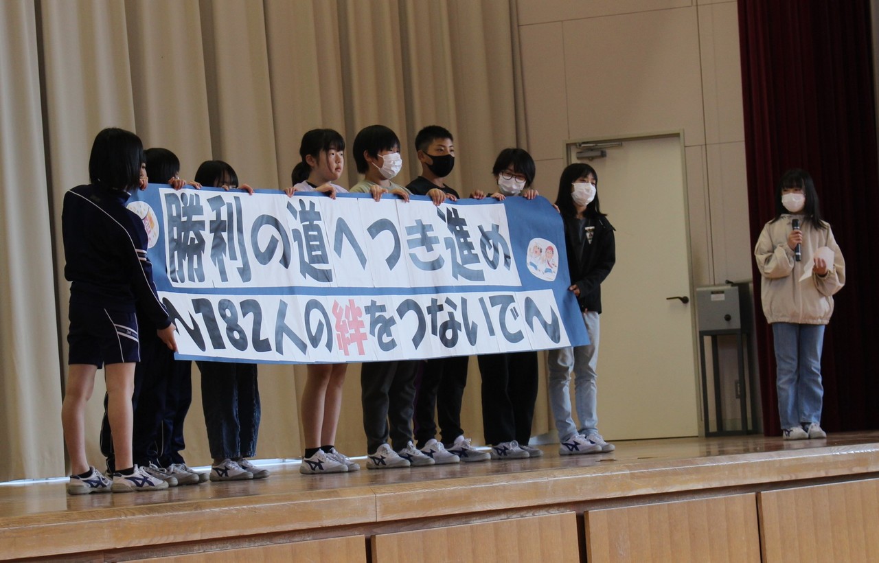 体育館のステージ上で勝利の道へ突き進めと書かれた幕を持っている児童たちの写真