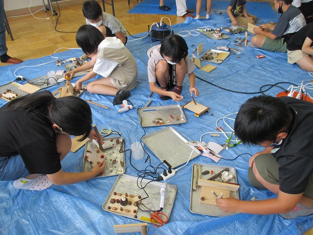 材料と道具を使いそれぞれ思い思いの木工クラフト作品を作っている児童たちの写真