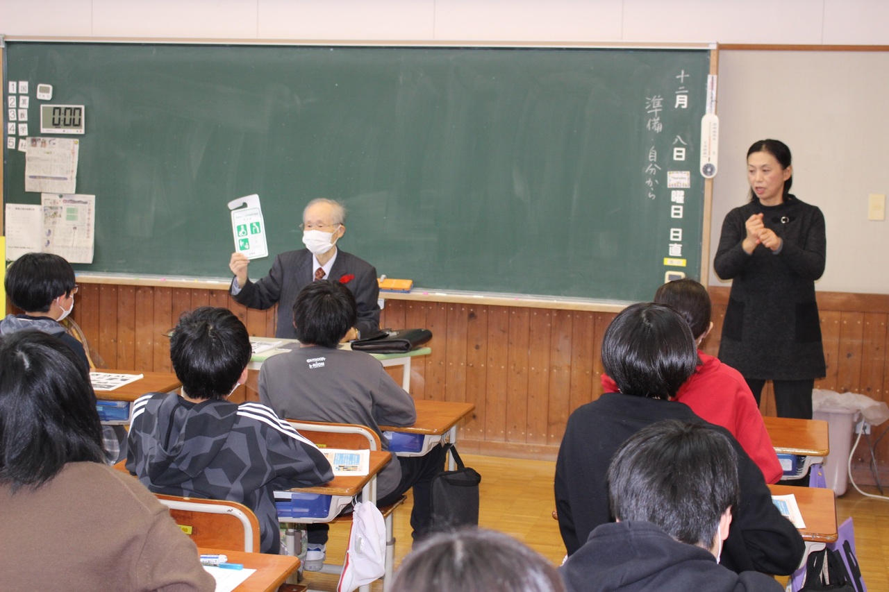 学校の教室で高齢の男性の話を聞いている児童たちの写真