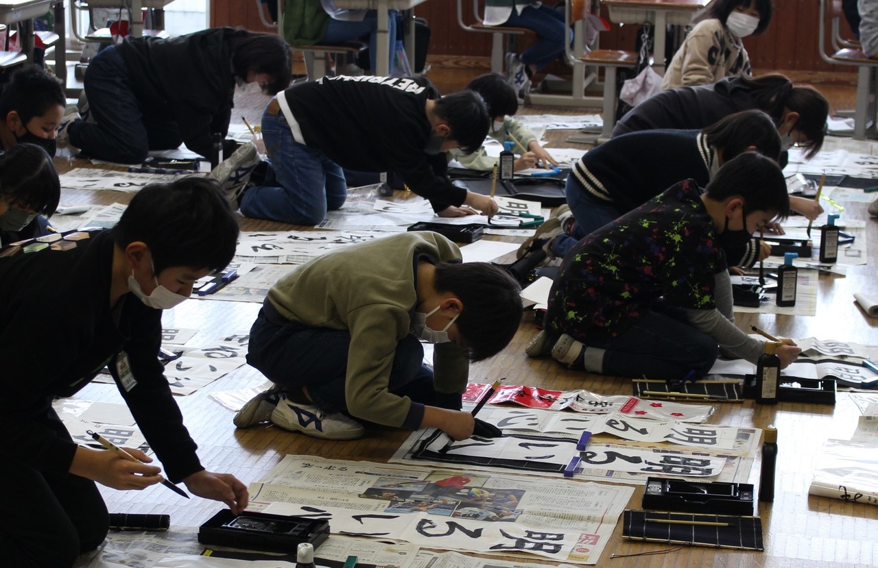 「明るい心」という文字を筆で書く子供たちの写真