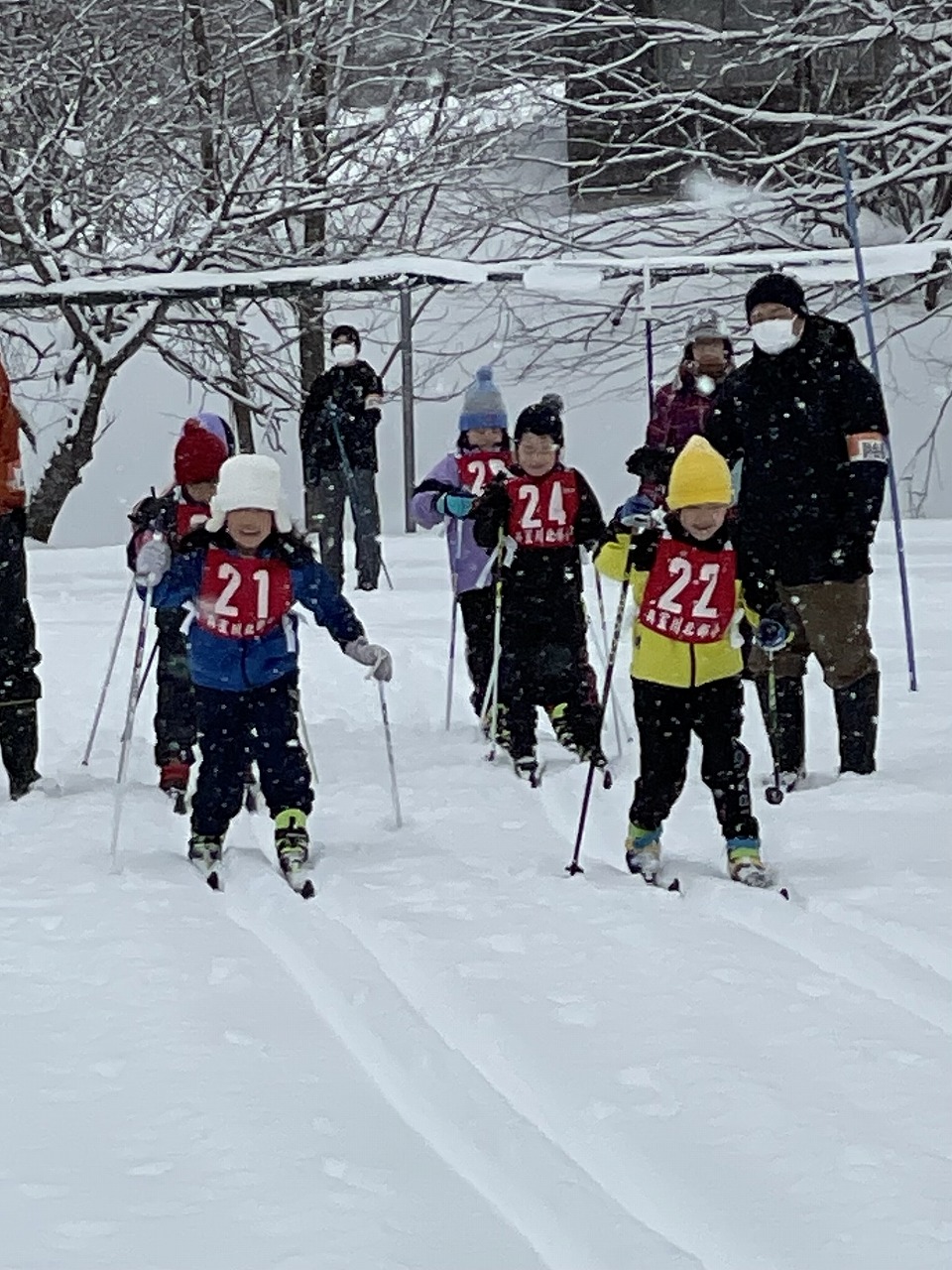 真室川北部小学校スキー大会にて、雪に覆われたスキー場で、スキー板に乗って滑走しようとしている低学年の複数人の児童達の様子を写した写真