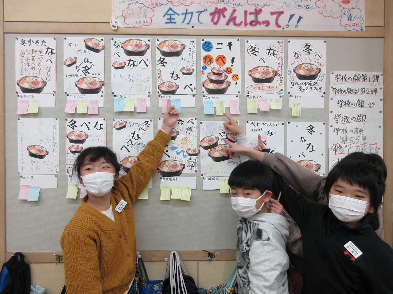 掲示板に並べられたポスターに自分のものがどれかを得意げに指さす生徒たちの写真