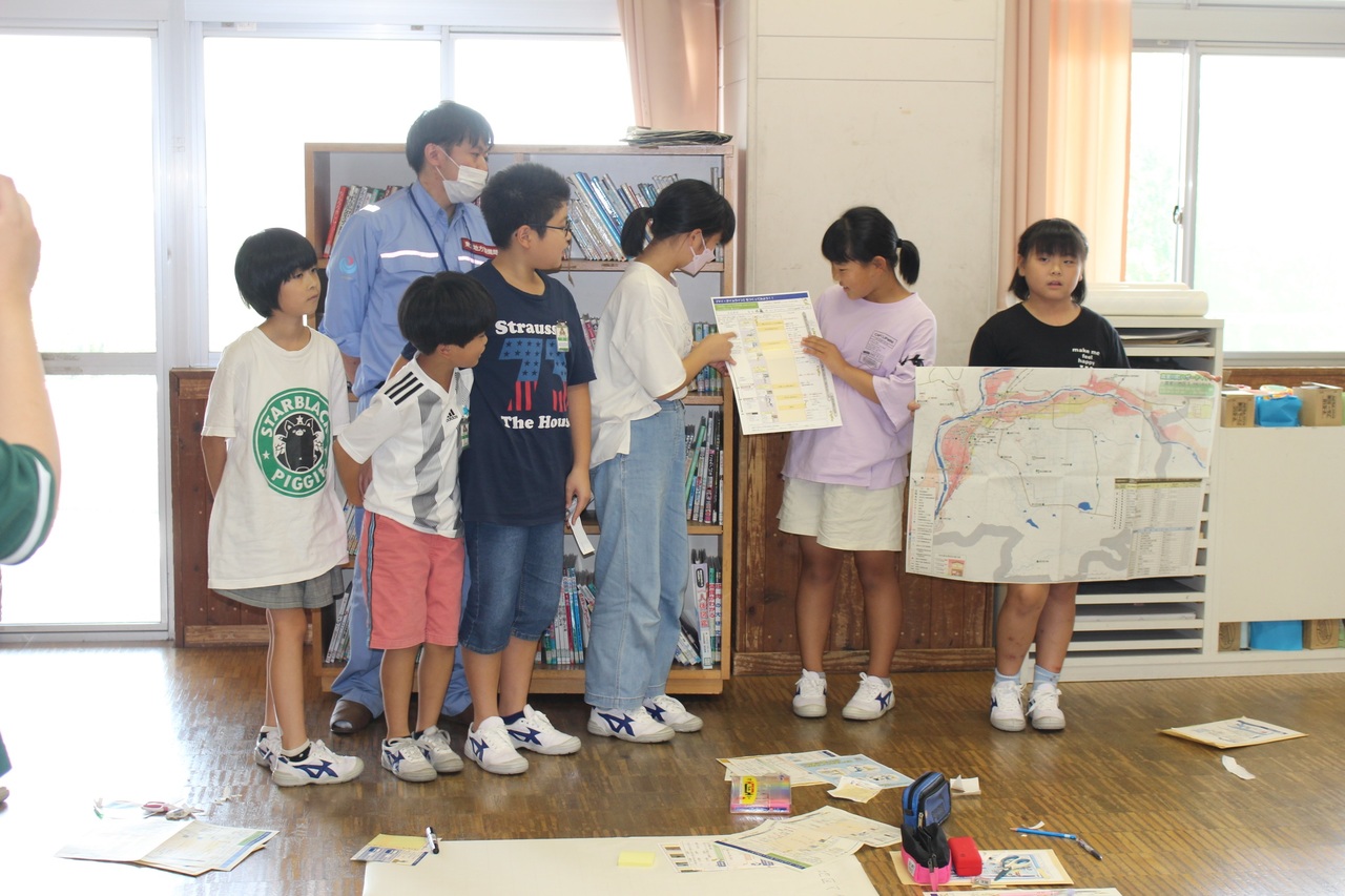 一列に並んで地図などを掲げ発表をする子供たちの写真