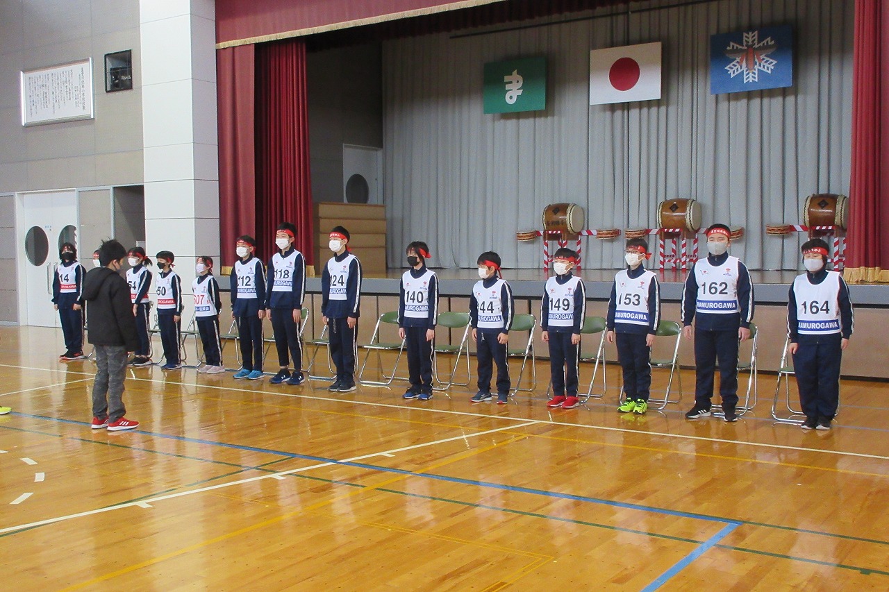 小学校の体育館で行われたスキー大会の壮行式にて、壇上の前に立つ、スキー大会に参加する14人の児童の様子を写した写真