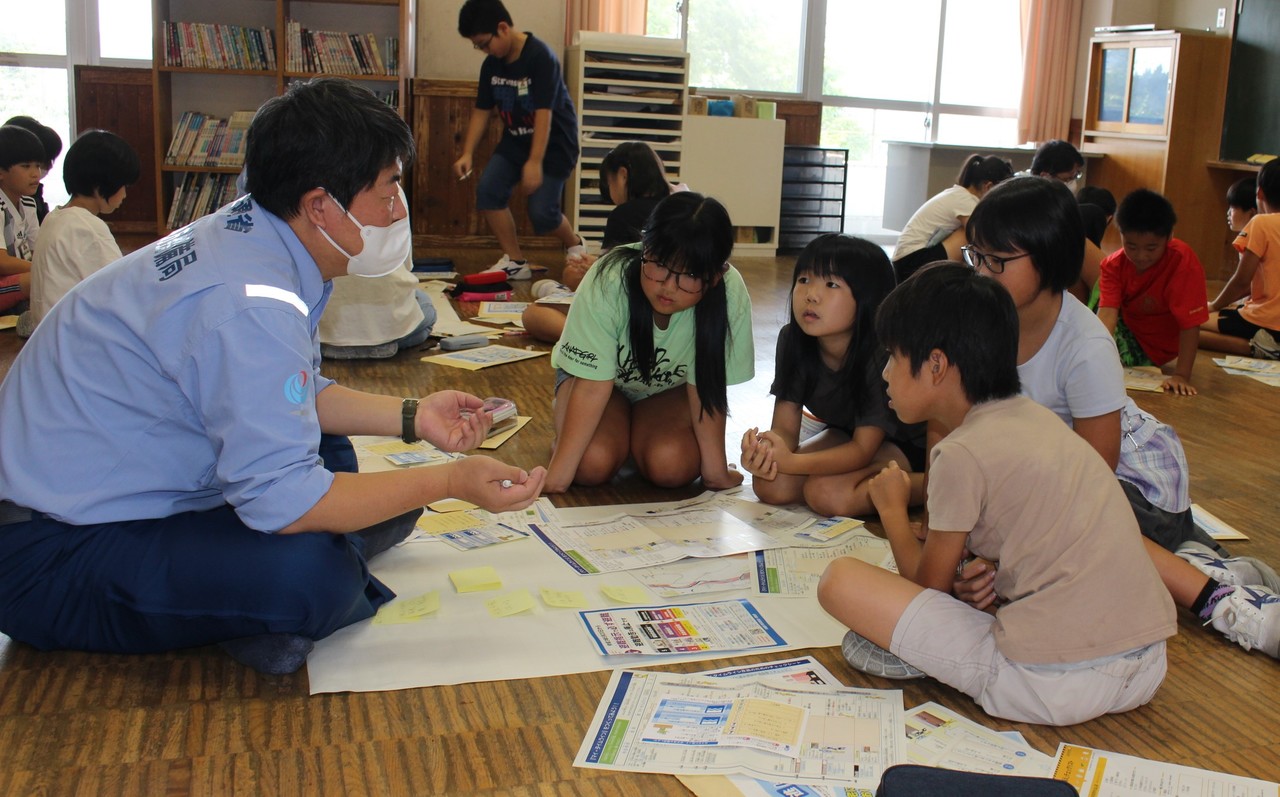 子供たちに話をしている水色のワイシャツ姿をした男性の写真