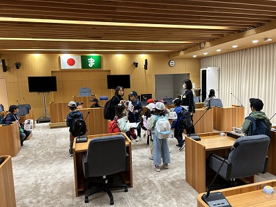 議場の中を散策している子供たちとその中で子供たちを見守る2名の女性の写真