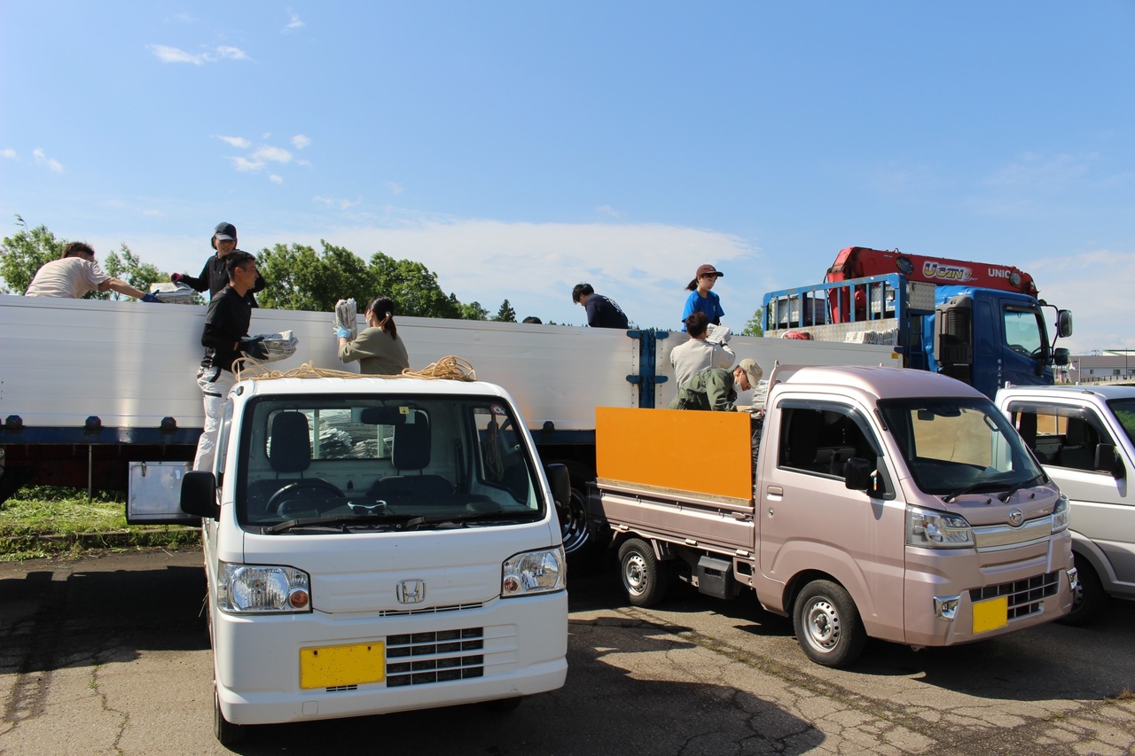 小型のトラックと大型のトラックとの間で荷物を積み替えている人々の写真