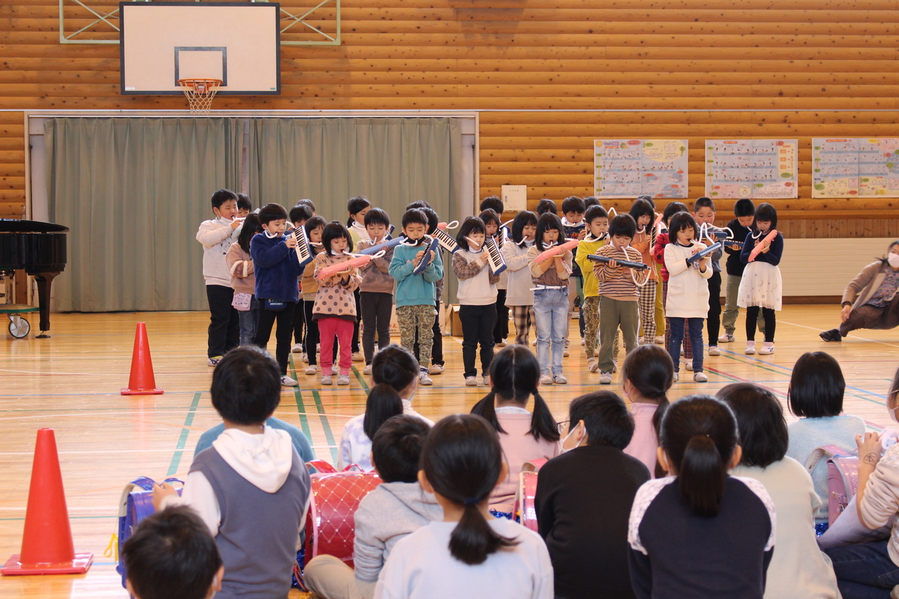 ピアニカを演奏する子供たちと体育座りでそれを眺める子供たちの写真