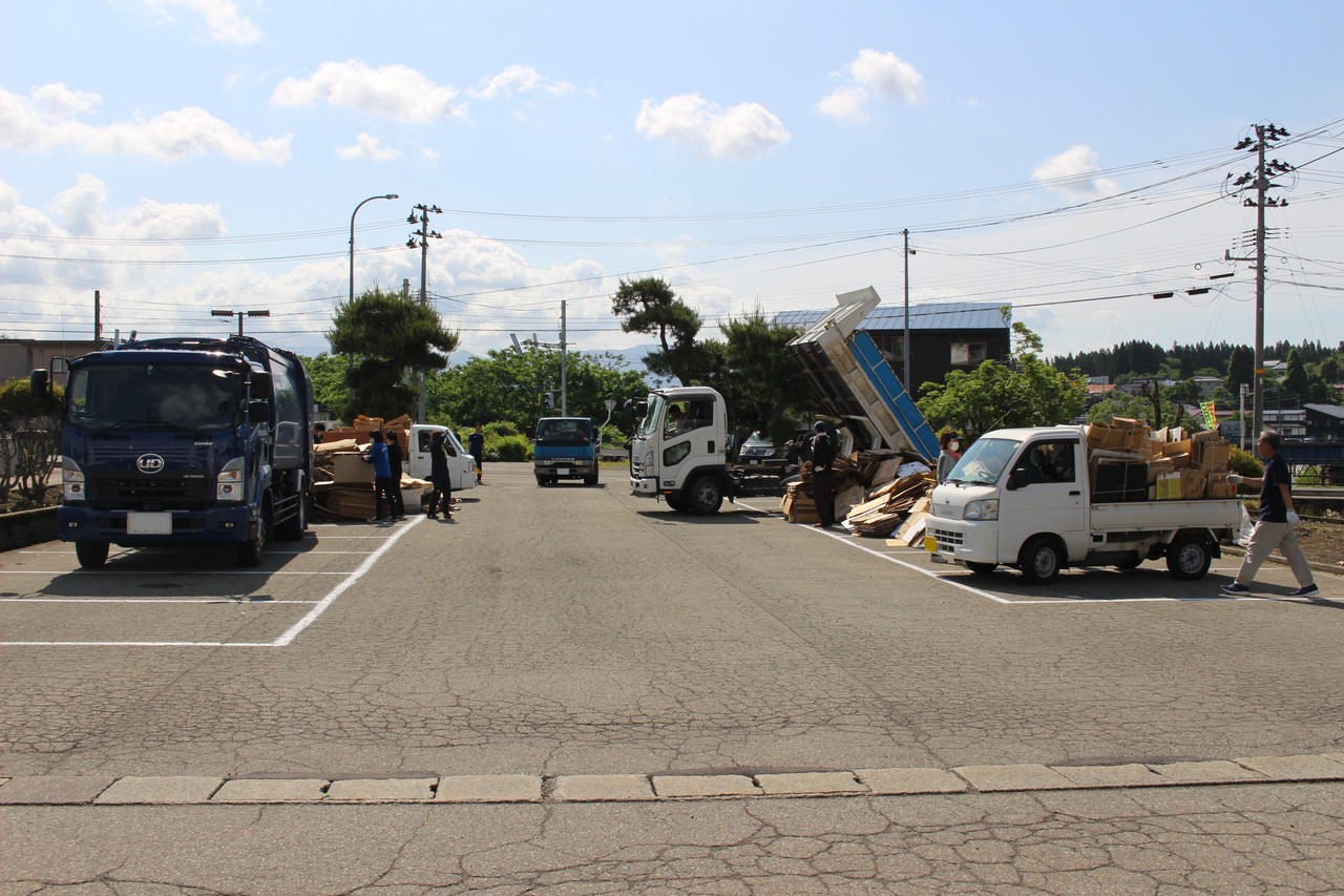 大量の段ボールなどの荷物を積んだ複数台のトラックが駐車場に停まっている写真
