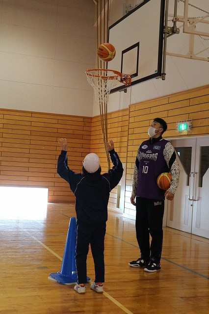 シュートの練習をする児童と、それを見守るプロ選手の写真