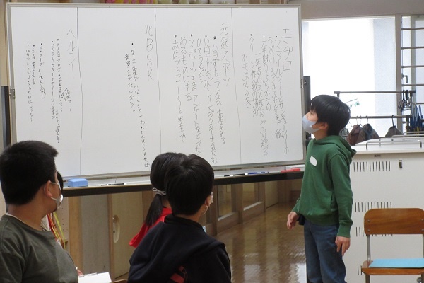 文章が書かれたホワイトボードの横に立つ男の子の写真