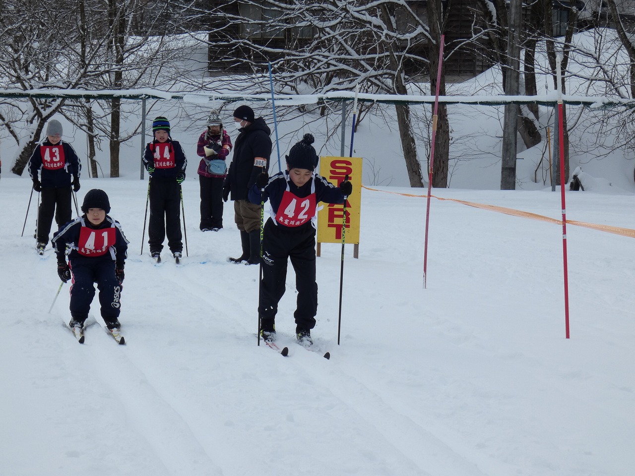 真室川北部小学校スキー大会にて、雪に覆われたスキー場で、スキー板に乗って滑走している4人の児童の様子を写した写真