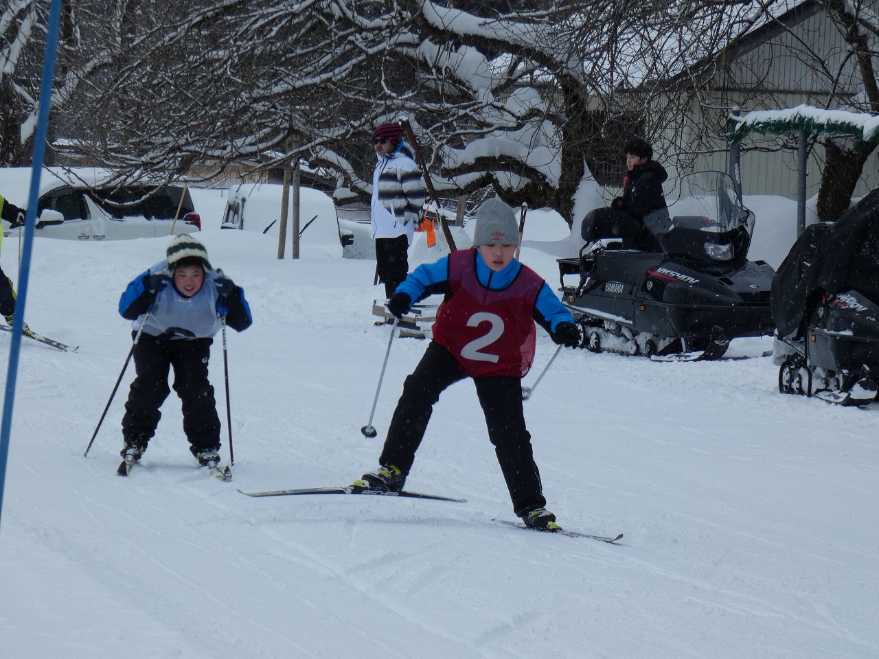 真室川北部小学校スキー大会にて、雪に覆われたスキー場でスキー板に乗って滑走している、赤の2番と白の6番のゼッケンをつけた男子児童2人の様子を写した写真