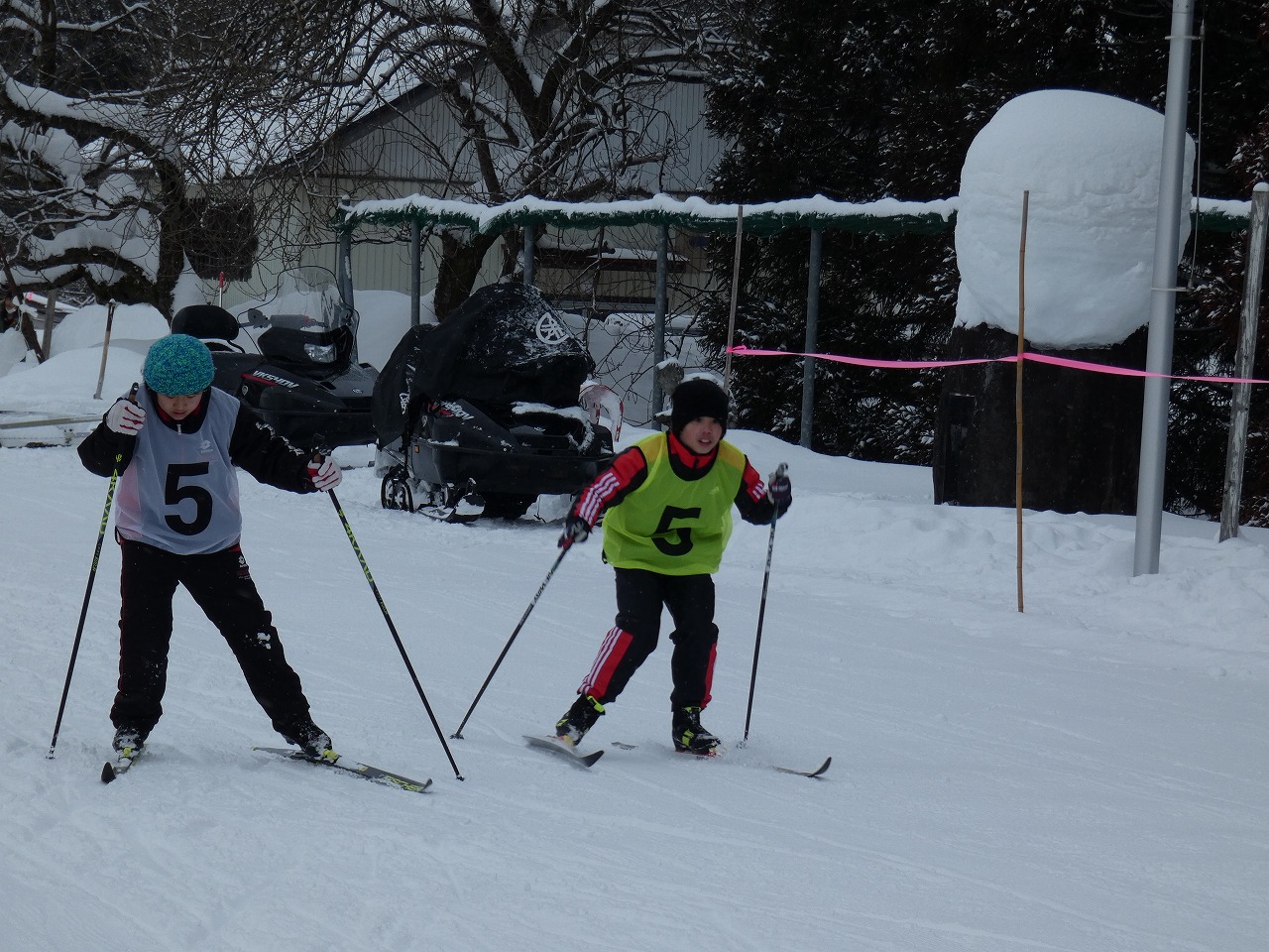 真室川北部小学校スキー大会にて、雪に覆われたスキー場でスキー板に乗って滑走している、緑の5番と白の5番のゼッケンをつけた男子児童2人の様子を写した写真