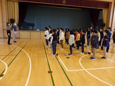 体育館で、起立した状態で、先生と英語でコミュニケーションの練習をする児童たちの写真
