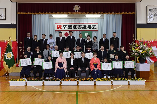 保護者と卒業生、校長・教頭・担任が、体育館の舞台の前に集合、整列して撮った写真
