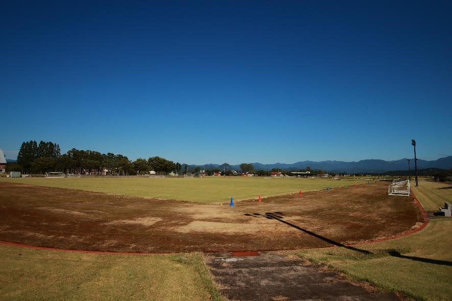 青い空の下、遠くに山並みを望む広々としたサッカー場の写真