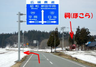 道路右手に祠があり、ここで左折する事を赤い矢印で記している道路の写真