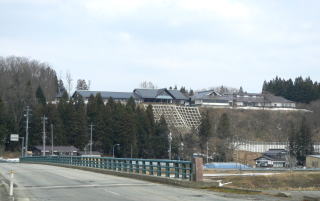 橋の先の丘に黒い屋根の建物が建っている写真