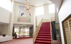 金色の手すりに赤色の絨毯が特徴的な階段が中央にあるロビーの写真