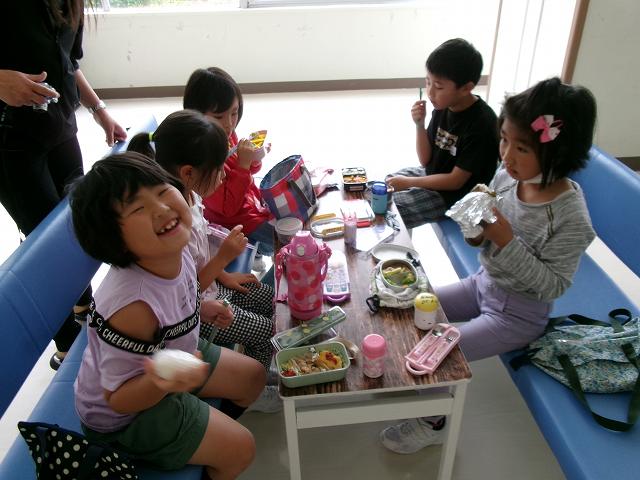 体育館ホールのテーブルにお弁当を広げ、楽しく食事をする児童たちの写真