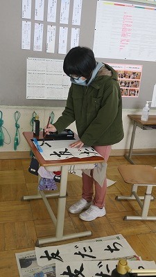 立って「友だち」という言葉を縦長の半紙に練習する3年生の女の子の写真