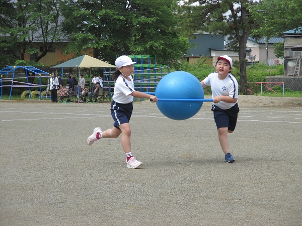 青い大玉を青い棒2本で挟んで2人で走って運んでいる写真