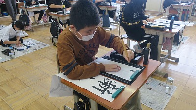 一生懸命書き初めをする左利きの5年生の生徒の写真