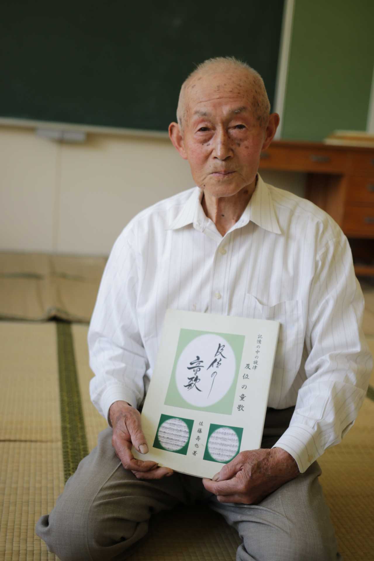 及位の童歌の冊子を持っている男性の写真